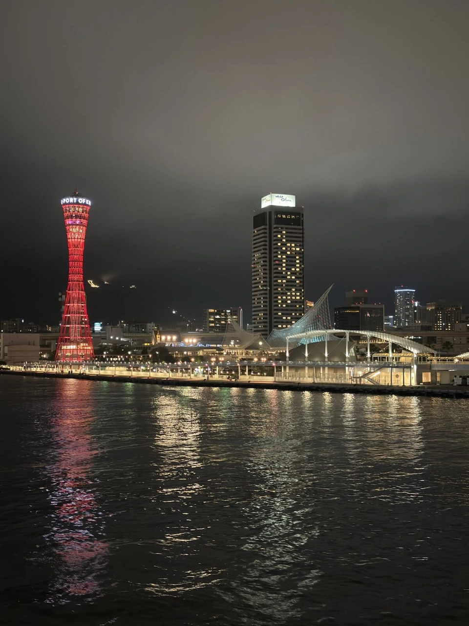 夜の神戸港。海面に映る赤いポートタワーと、隣のホテルの高層棟、海洋博物館
