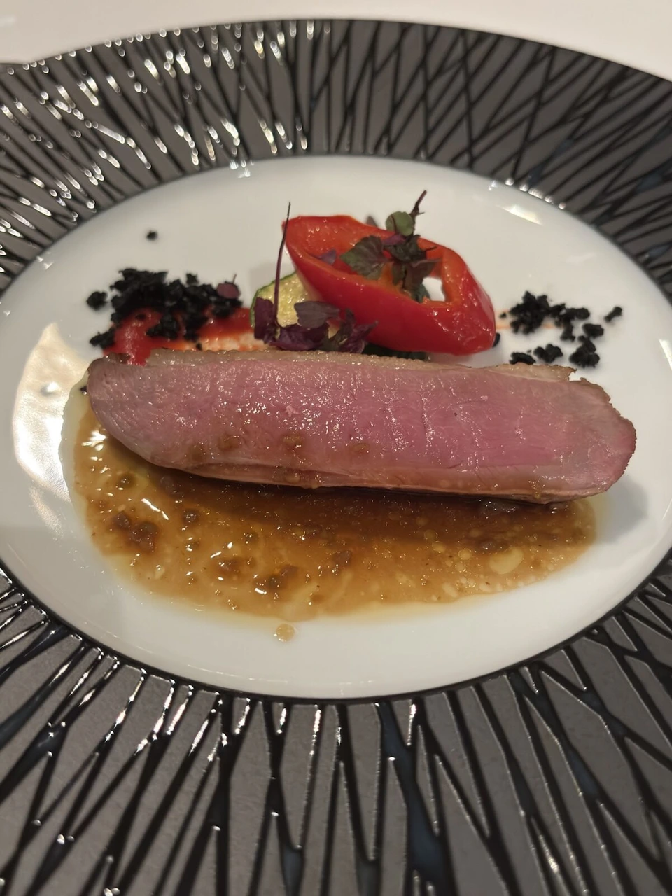 神戸港ディナークルーズのメインのお肉。断面がピンク色で、ソースと赤いパプリカ、黒いクランブルが添えてある