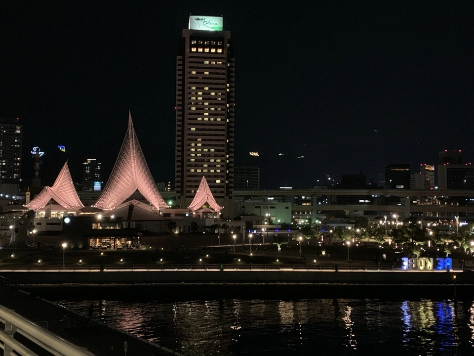 夜の海ごしに見た神戸海洋博物館の白い帆のような屋根と、その奥のホテルオークラ神戸の高い建物。水面に明かりが映る