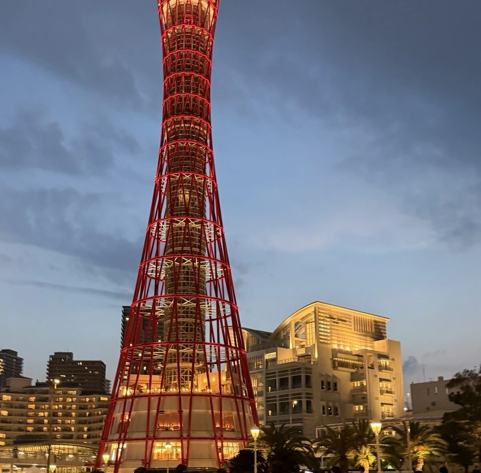 夕暮れの空に赤くライトアップされた神戸ポートタワーと、右の明かりのついたホテル