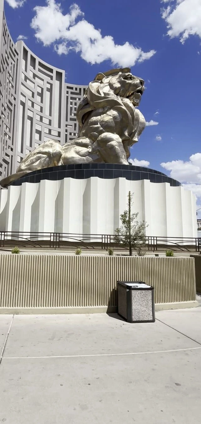 MGMグランドの前の台座に座る金色のライオンの像と、後ろの格子模様の外壁