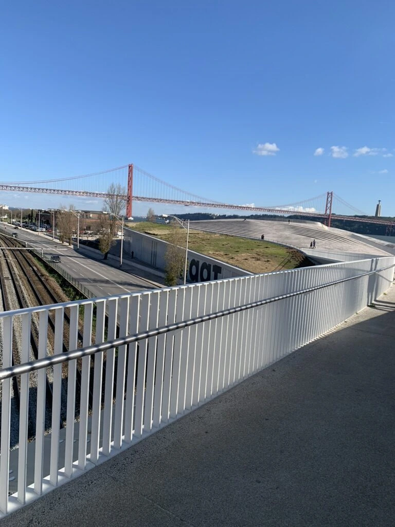 MAATの屋上へ続く白い手すりの歩道橋と、下を通る線路