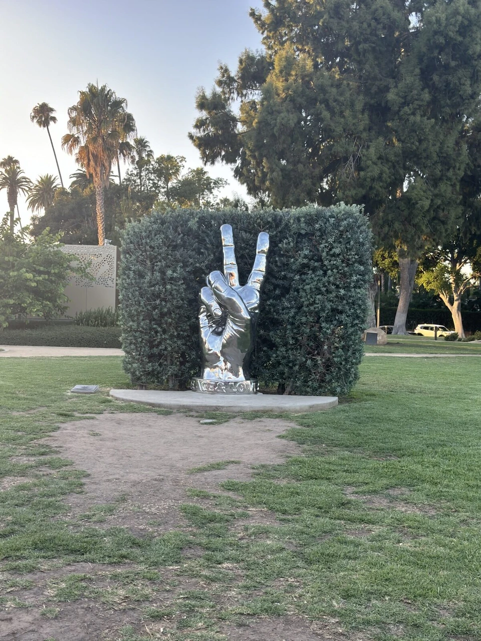 ビバリーヒルズの公園の植え込みの前に置かれた、ピースサインの手の銀色の彫刻
