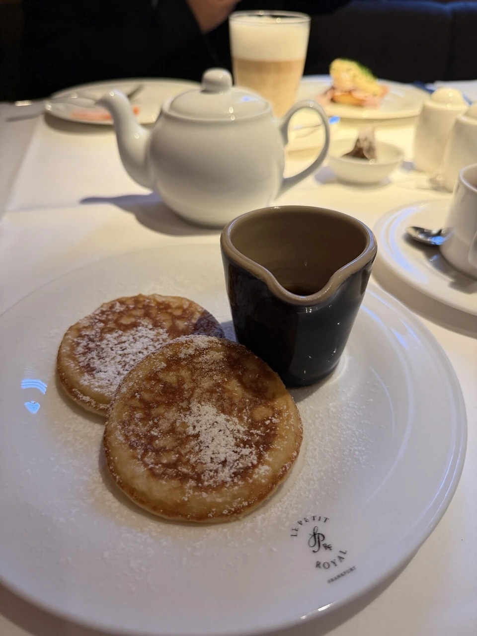 LUMEブティックホテルのレストランの朝食。小さなパンケーキ2枚と黒いピッチャー、奥に白いティーポット