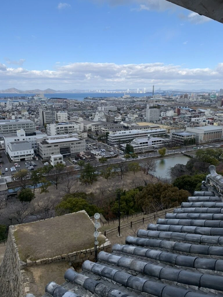 天守の窓から見た瓦屋根の先の市街地と海