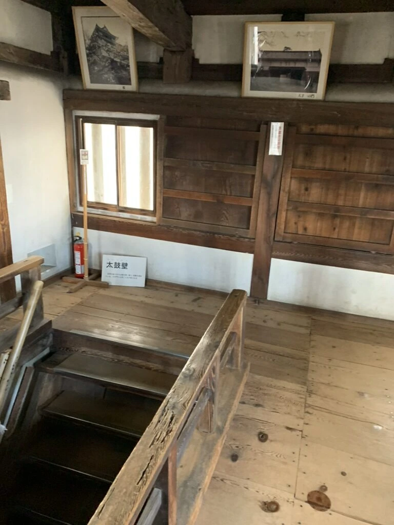 丸亀城天守の中の板張りの部屋と、下の階へ降りる階段、壁に掛けられた古い写真