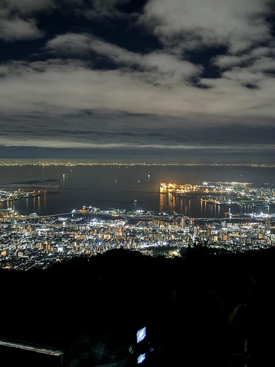 掬星台からの夜景。海に突き出た埋め立て地の明かりと、手前の街の明かり、上に雲の多い空