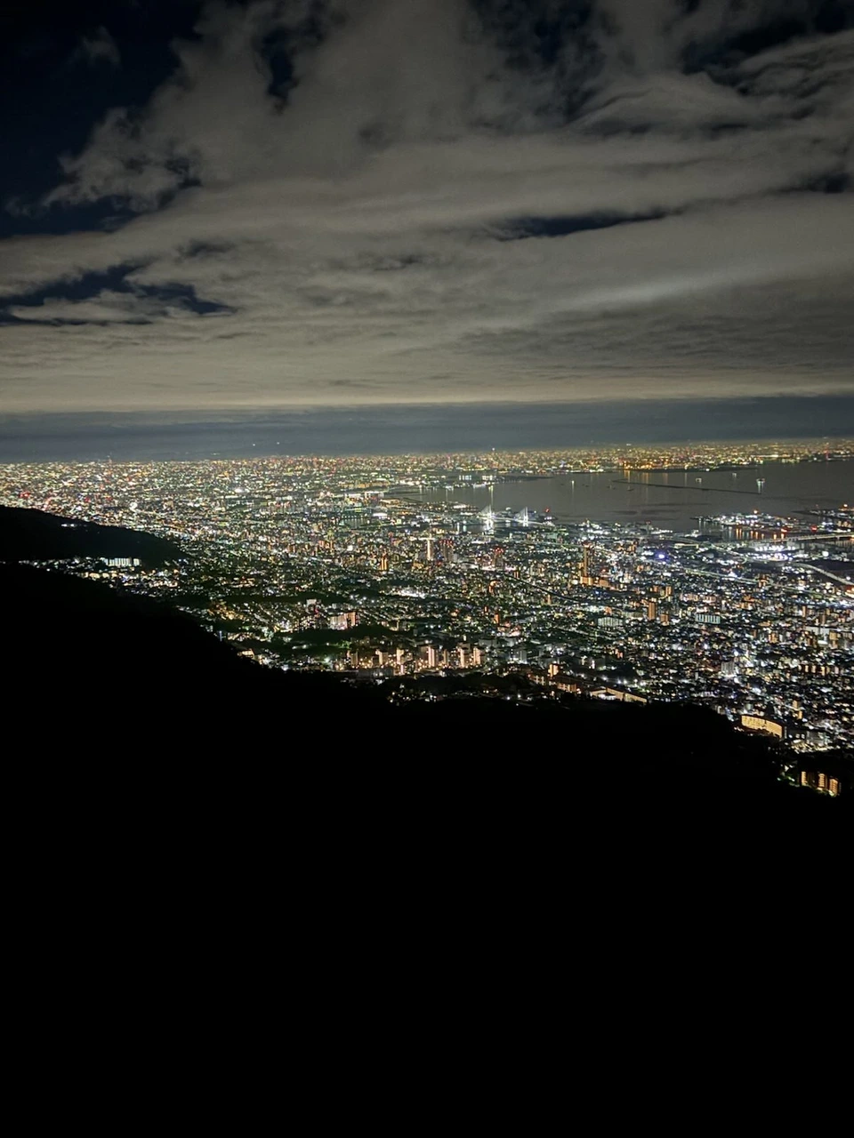 掬星台から見下ろした夜景。雲の多い空の下、山すそから海沿いまで神戸の街の明かりが帯のように続く