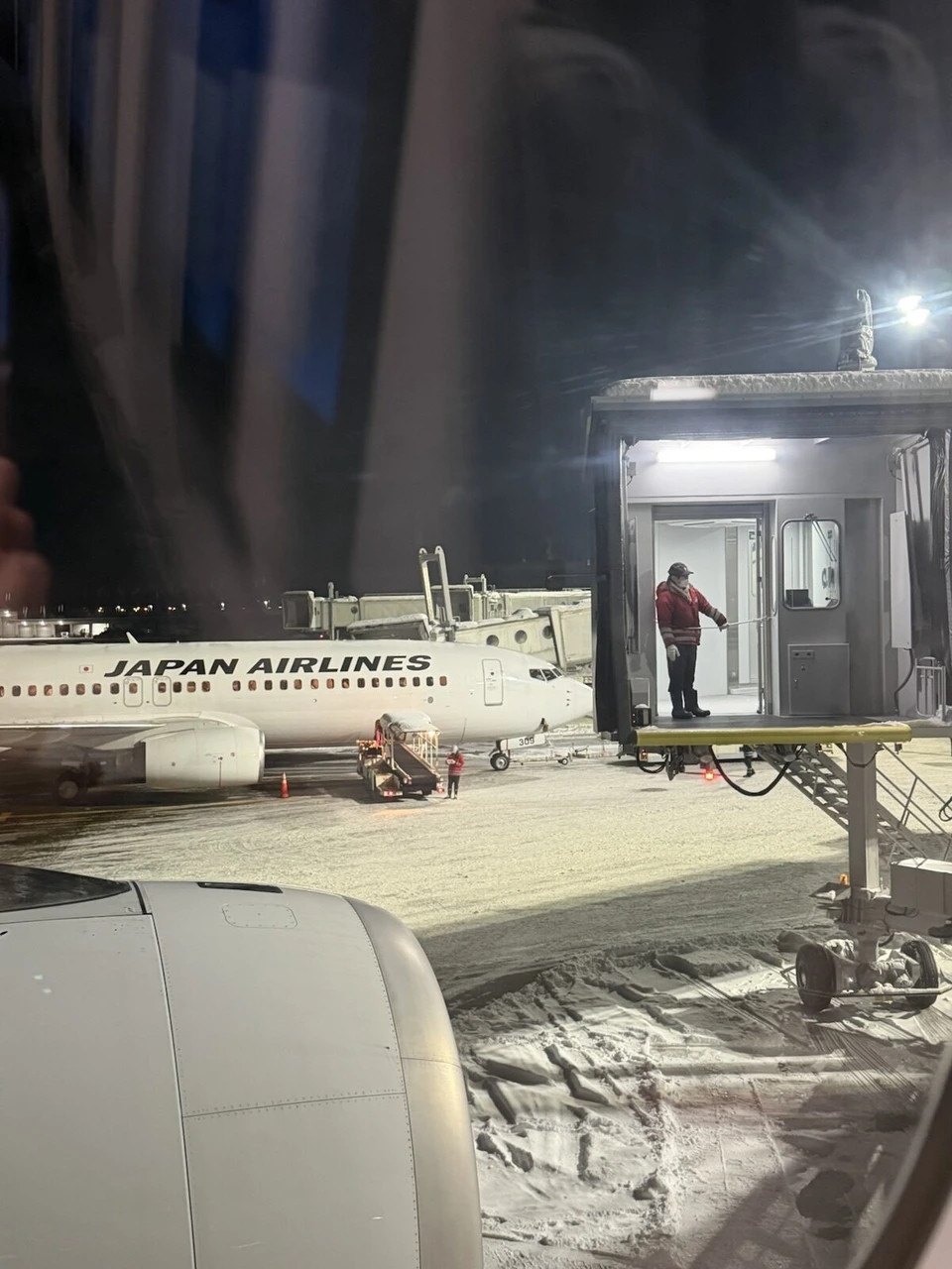 夜の新千歳空港に着いた機内の窓から見た景色。雪が積もった駐機場に止まるJALの737と、照明に照らされたボーディングブリッジ