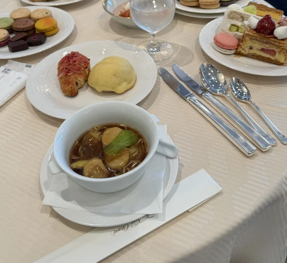 丸いテーブルの上の1皿目。いちごをのせたクロワッサン風のパンとメロンパン風のパン、野菜の入ったスープ、奥にマカロンやケーキの皿