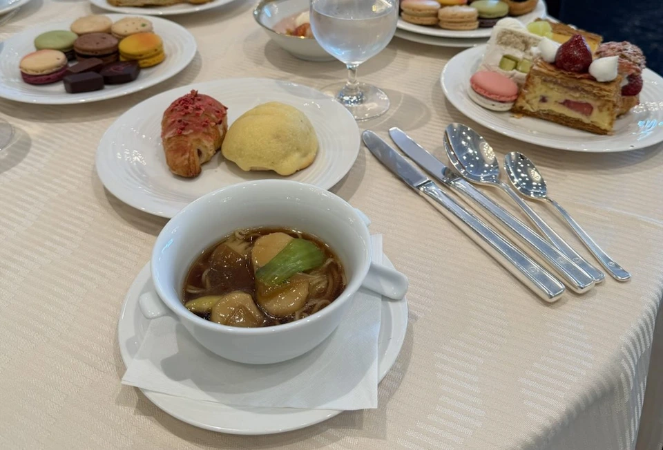 丸いテーブルに並んだお皿。手前にパン2つとスープ、奥にマカロンとチョコレートの皿、いちごのミルフィーユのようなケーキの皿