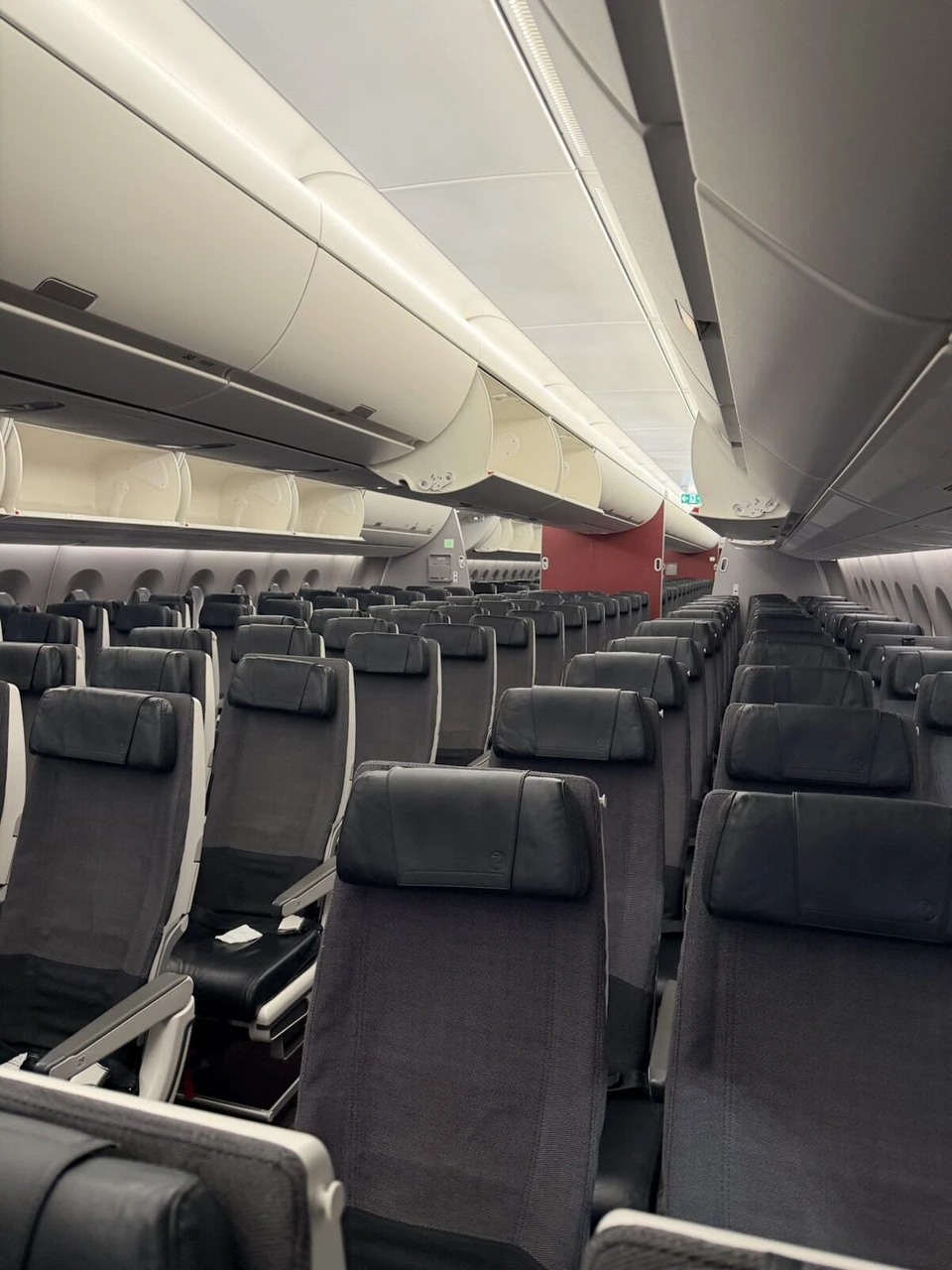 JALの飛行機の普通席の通路。黒い座席が並び、上に荷物入れ