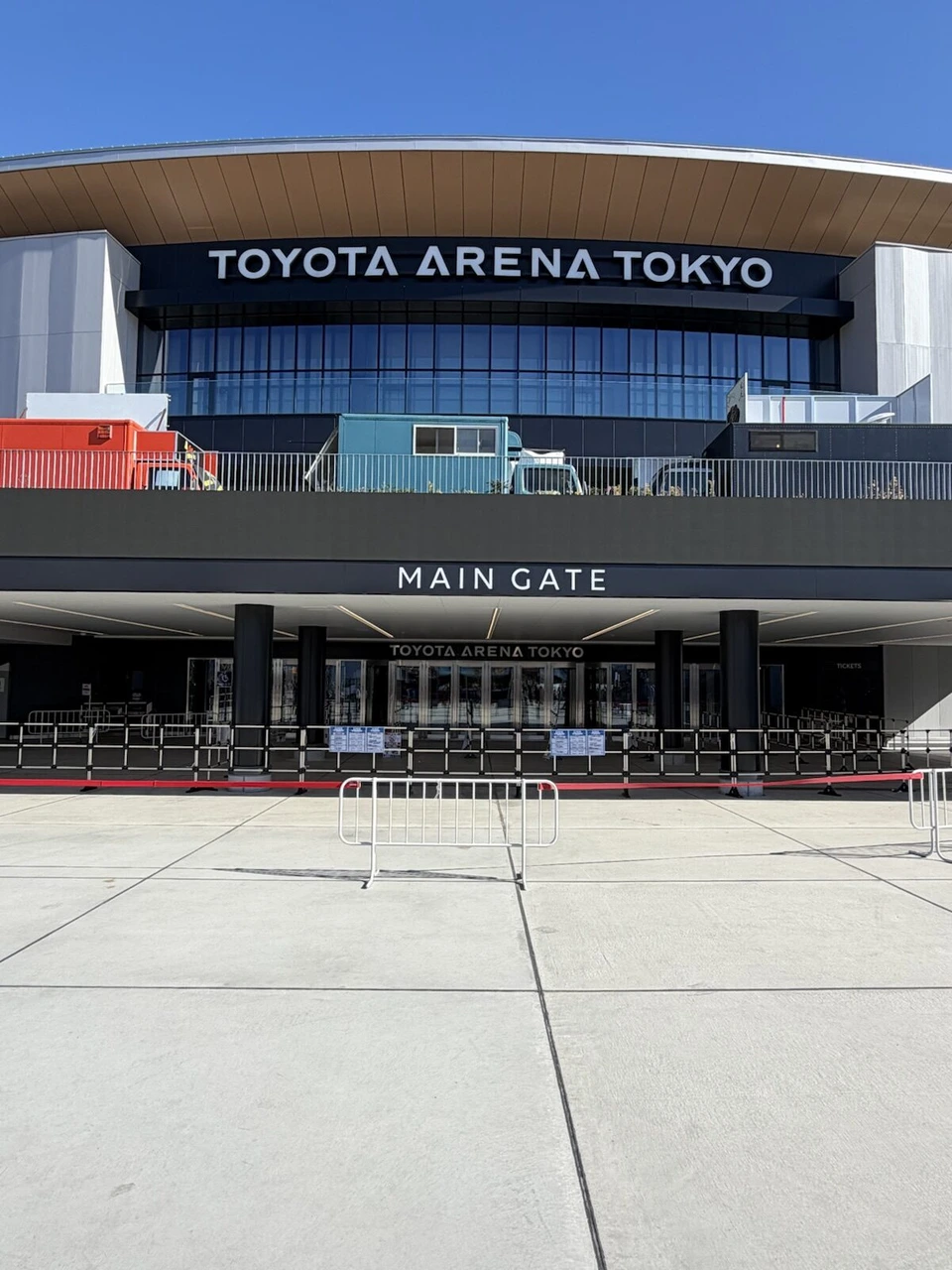 青空の下のTOYOTA ARENA TOKYOの正面。MAIN GATEの文字と入口の柵、2階のテラスにキッチンカー