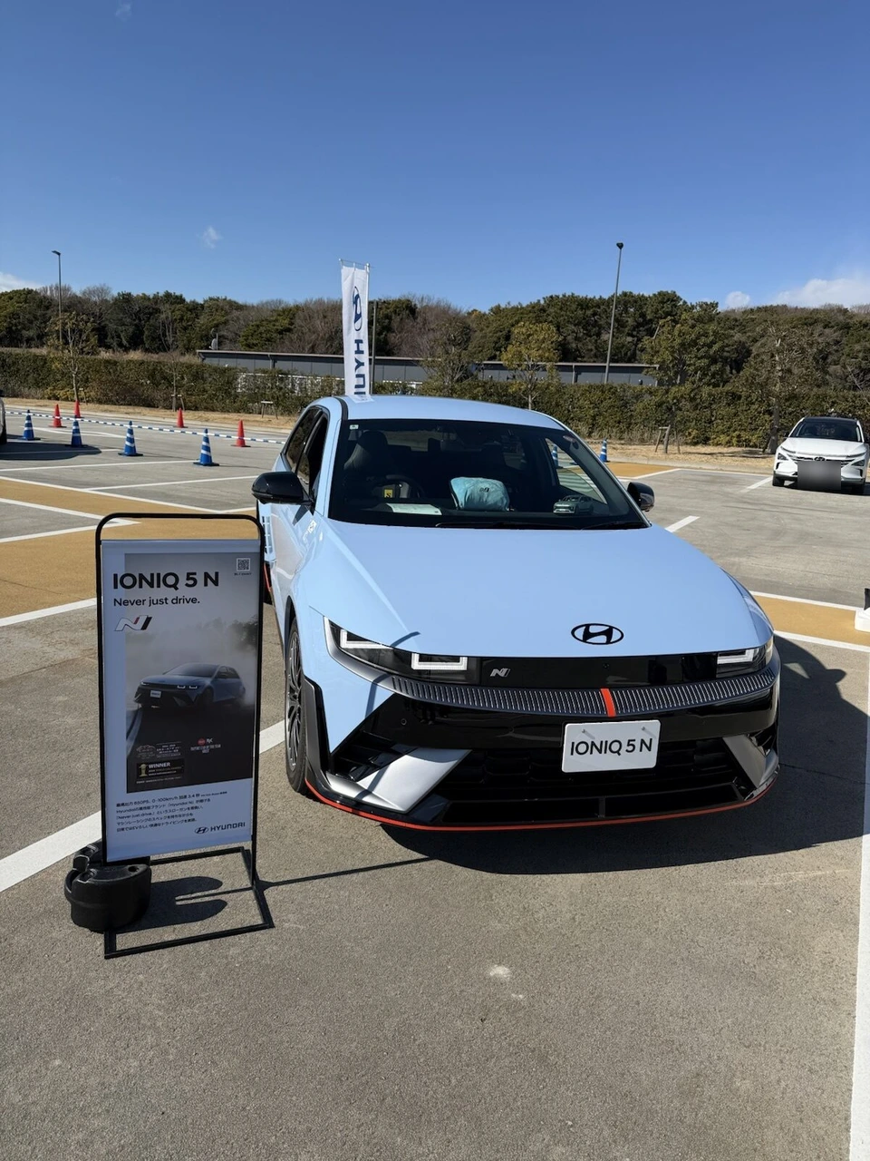駐車場に展示された水色のヒョンデ アイオニック5 N。横に車の説明の看板と、奥にパイロンで仕切ったコース