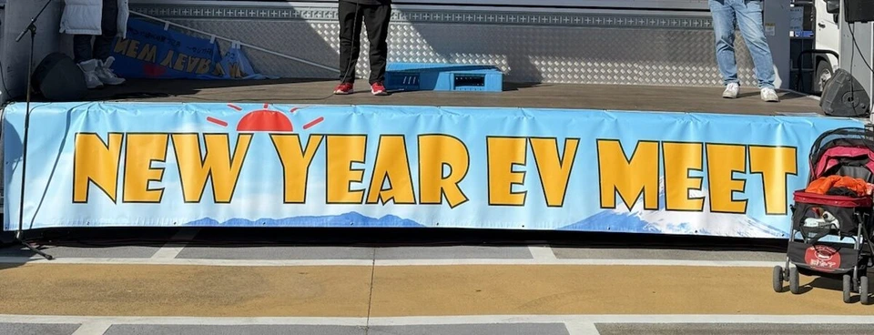 トラックの荷台を使ったステージ。手前に黄色い文字でNEW YEAR EV MEETと書かれた青い横断幕