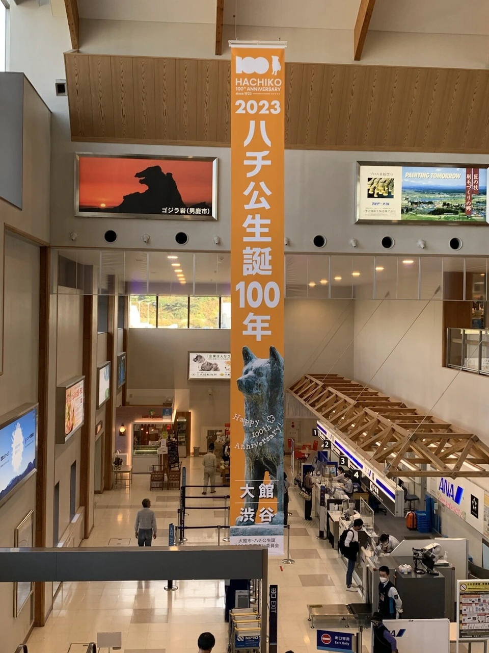 大館能代空港の上の階から見下ろした1階のチェックインロビー。オレンジ色のハチ公生誕100年の縦長の幕と、ANAのカウンター、木の梁の天井