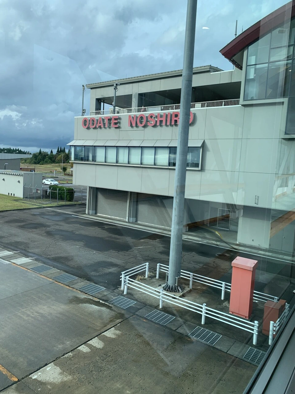 大館能代空港の搭乗待合室の窓から見たターミナルの端。外壁に赤い文字でODATE NOSHIRO、空は雲が多い