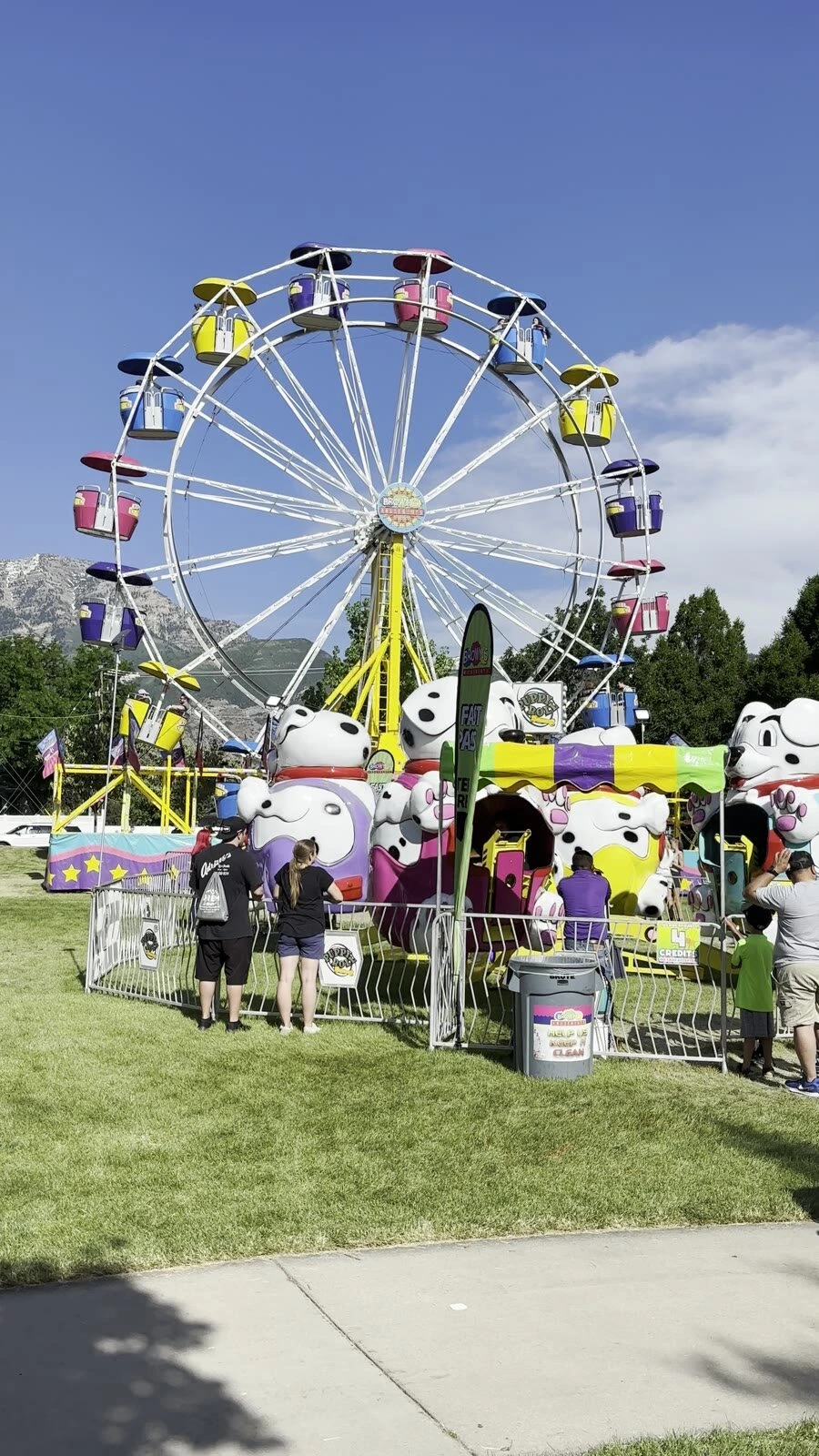 オレムフェストの芝生の会場に建つ観覧車と、白い犬の形をした子ども向けの乗り物、奥の山