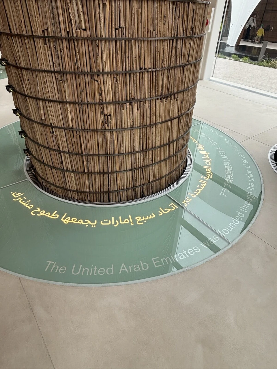 UAE館の細い木の棒を束ねた太い柱と、足元の円形の床に書かれたアラビア語と英語の文字