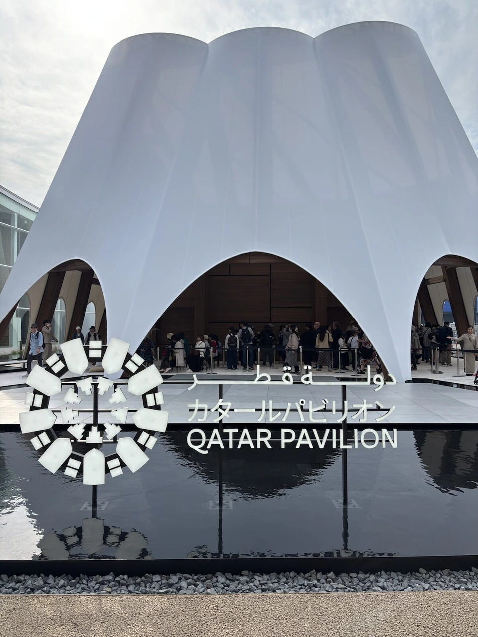 白い帆のような屋根のカタール館と、水面の前のQATAR PAVILIONのロゴ