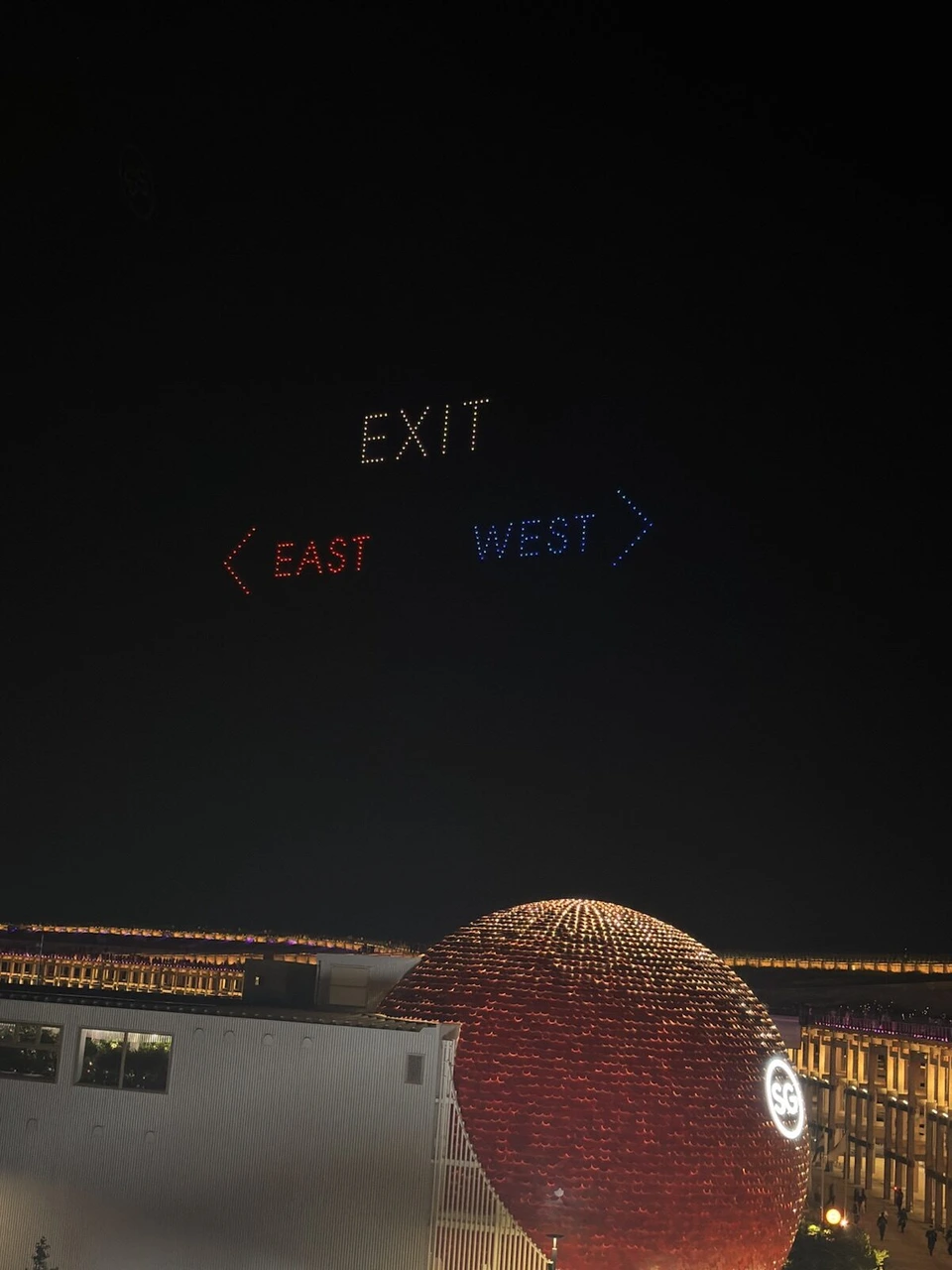 夜空にドローンで描かれたEXITの文字と、左向きのEAST、右向きのWESTの矢印