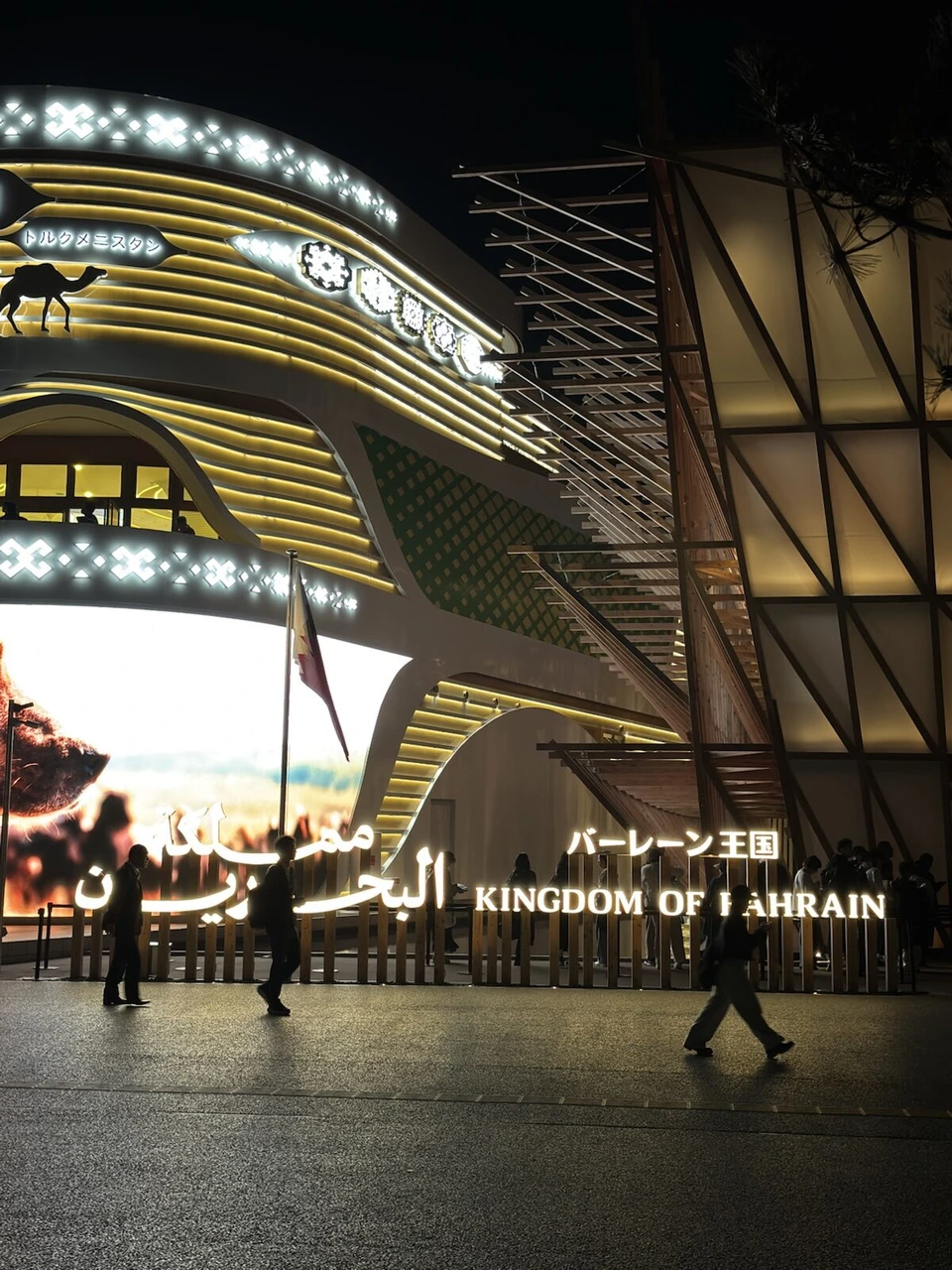 夜のバーレーン王国館。木の帆を重ねたような外観と、金色に光る入口、KINGDOM OF BAHRAINの文字
