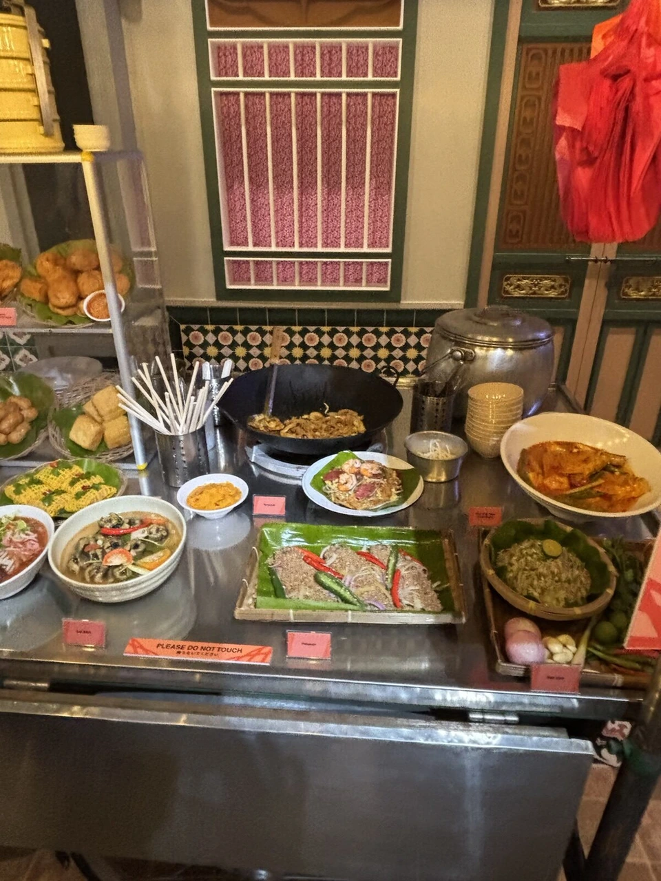 屋台風のカウンターに並ぶマレーシア料理の見本。中華鍋や皿に盛った料理