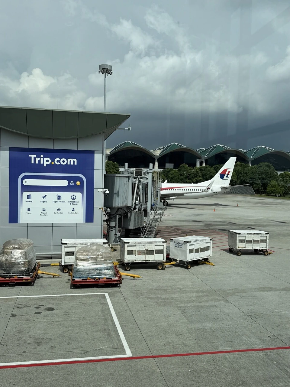 クアラルンプール国際空港の搭乗口の窓から見たマレーシア航空の機体とTrip.comの広告