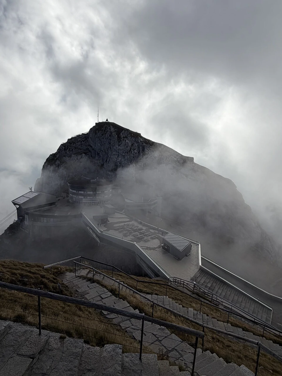霧に包まれたピラトゥス・クルムの山頂駅の建物と遊歩道