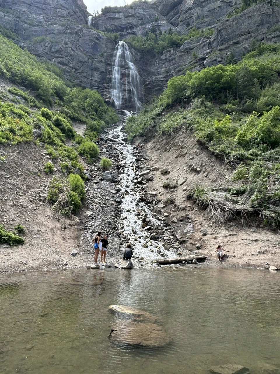 ブライダルベール滝の真下の岩場に立つ人と、水面に映る滝