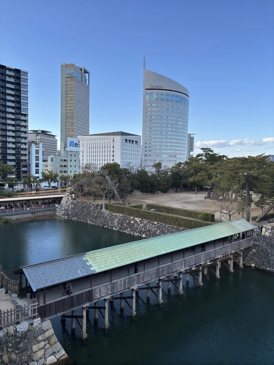 鞘橋と内堀、石垣。奥にサンポート高松の高層ビル2棟と青空
