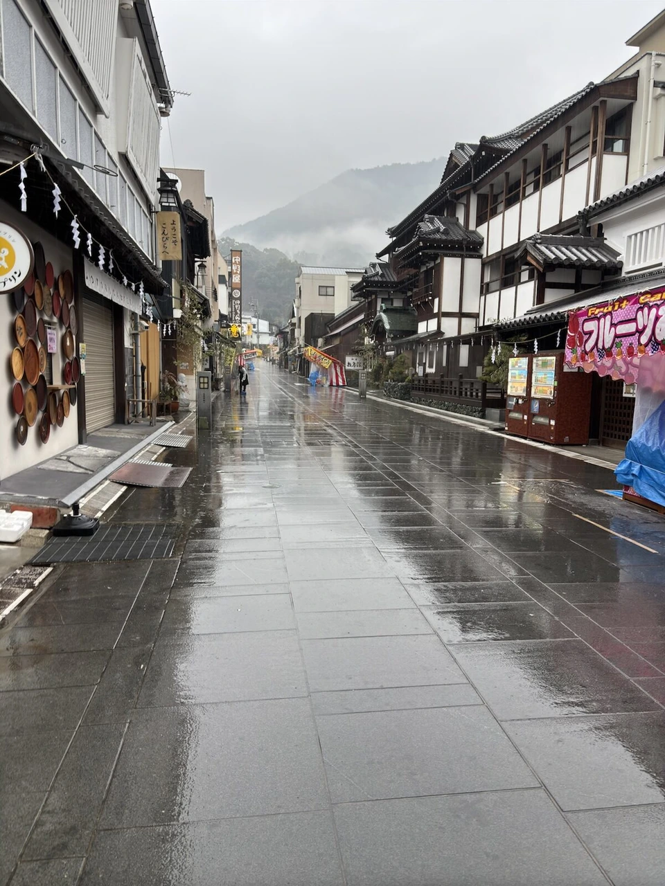 雨に濡れた琴平の参道。両側に土産物店や旅館が並び、奥の山に雲がかかっている