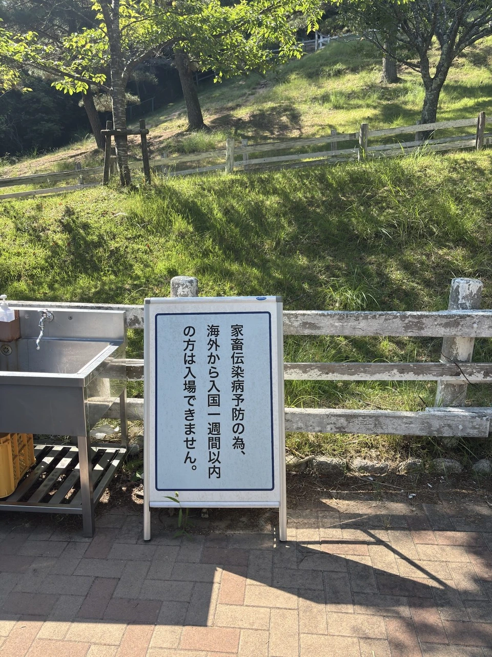 六甲山牧場の手洗い場の横に立つ看板。家畜伝染病予防の為、海外から入国一週間以内の方は入場できません、と書いてある