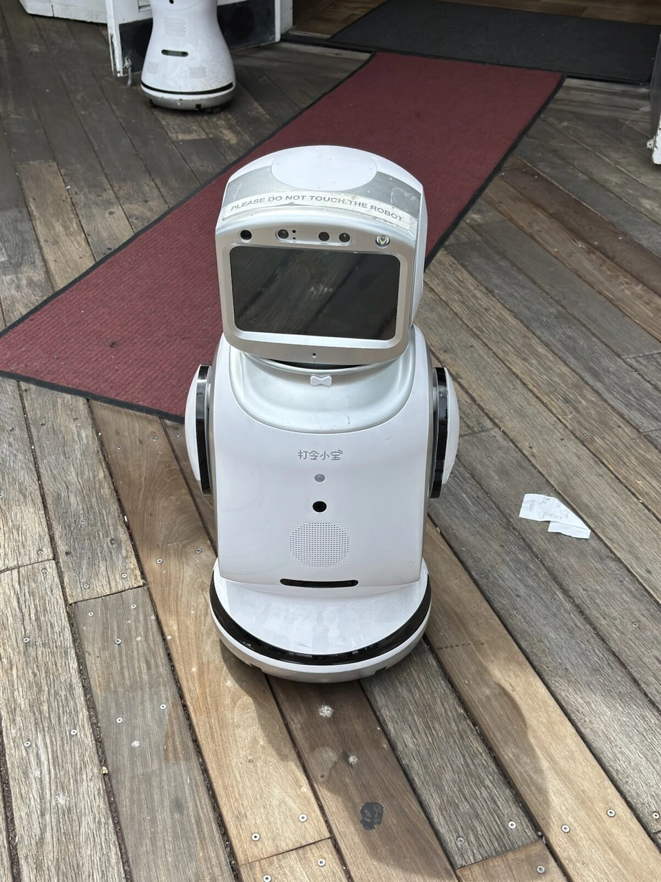 ピア39の木の床の上を動く、顔のような画面がついた白いロボット