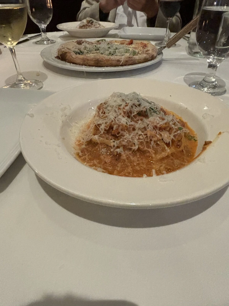 サンフランシスコのイタリアンで食べた、白いテーブルクロスの上のトマトソースのパスタと奥のピザ