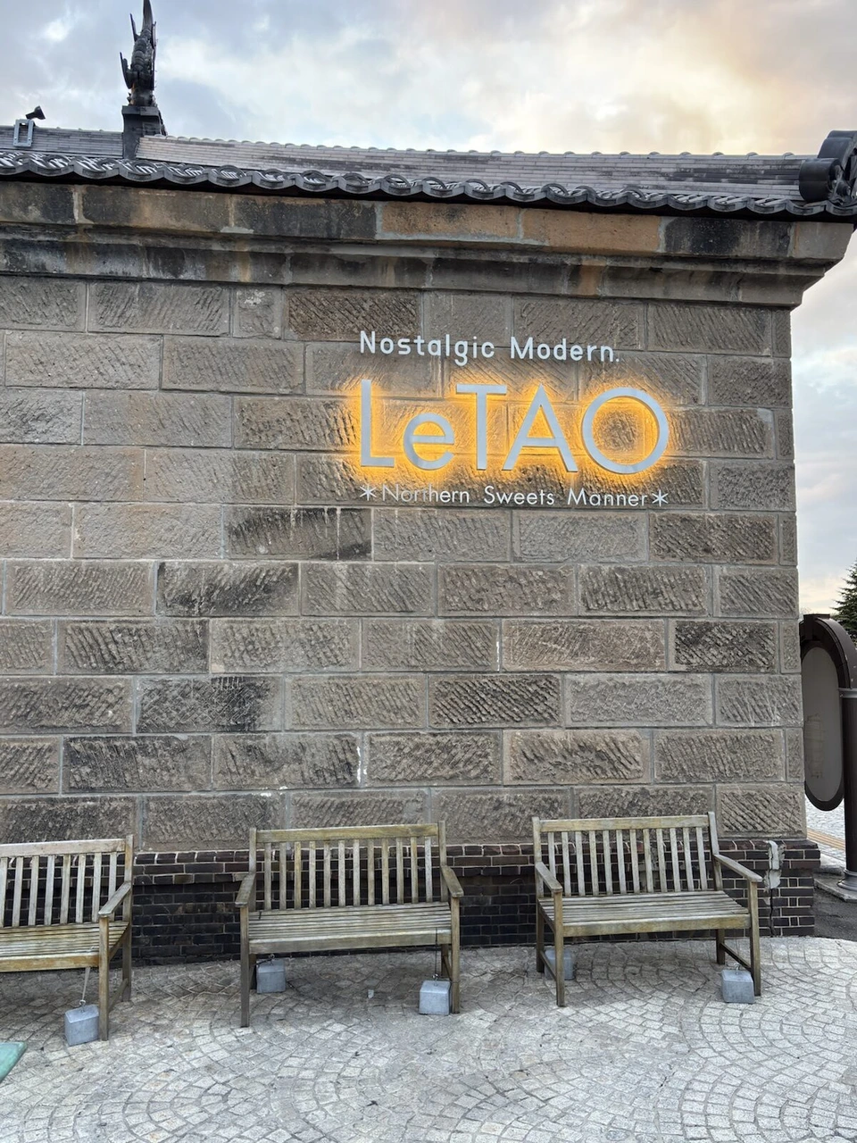 小樽運河近くの石造りの建物の壁にNostalgic Modern LeTAOの看板とベンチ