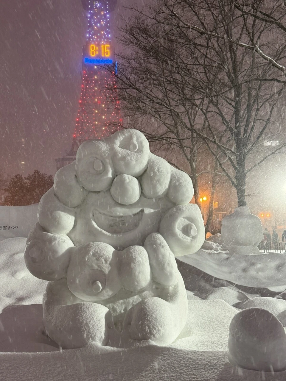 雪が降る中の丸い粒が集まったような形の雪像。奥にさっぽろテレビ塔
