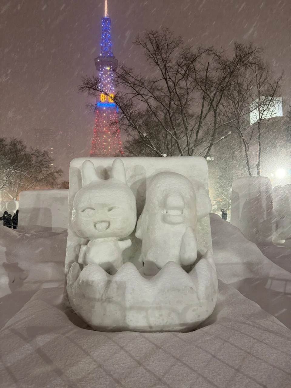 雪まつり大通会場2丁目の、2人のキャラクターが並ぶ市民雪像と、奥のライトアップしたテレビ塔