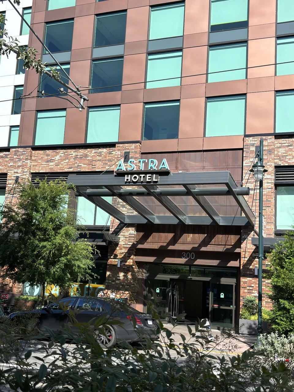 ASTRA HOTELの看板がある車寄せ。低層はレンガ、上は赤茶とミント色のパネルの建物