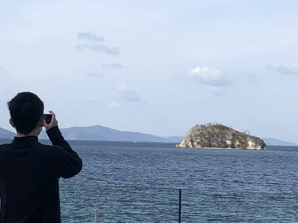 海に浮かぶ小さな岩の島を撮る人の後ろ姿