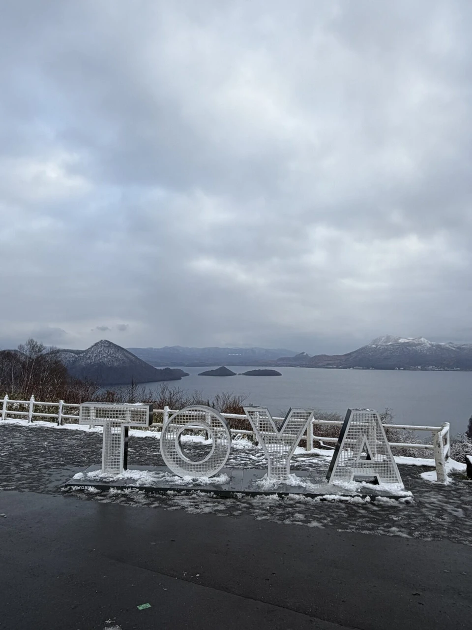 雪が残るサイロ展望台のTOYAの文字のモニュメントと、その向こうの洞爺湖と中島
