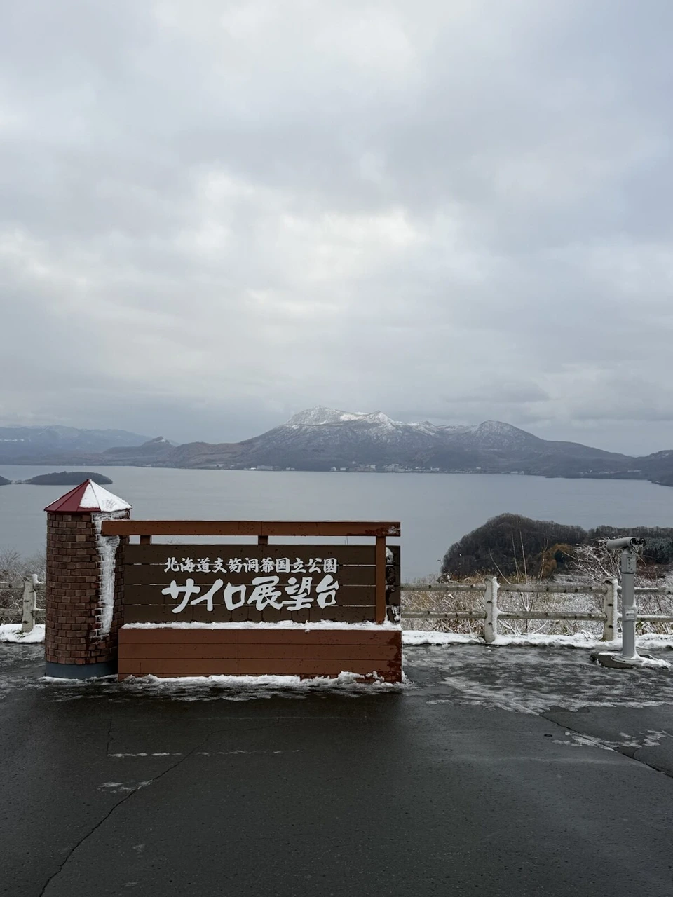 洞爺湖のサイロ展望台の看板と、その向こうの洞爺湖と雪をかぶった有珠山方面の山