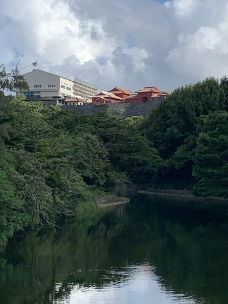 木々に囲まれた龍潭の水面と、奥の首里城の石垣と赤い建物