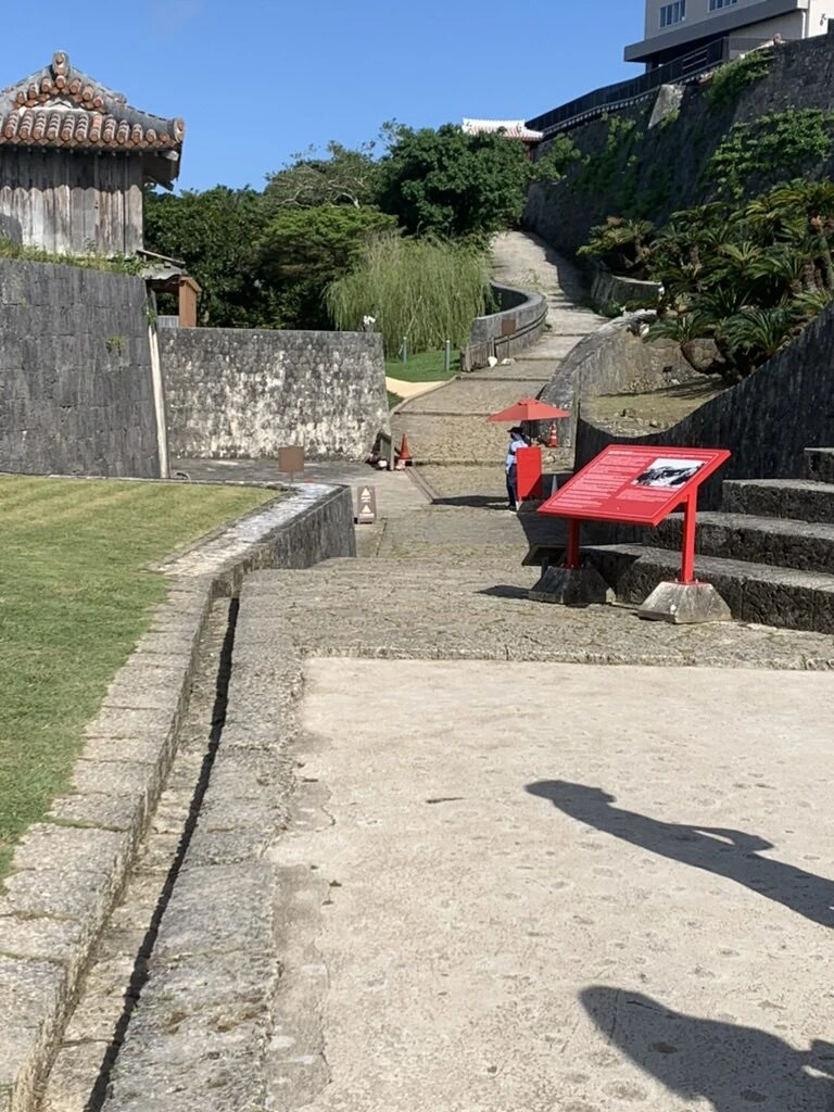 首里城公園の石垣の間を上っていく石畳の坂道と赤い案内板
