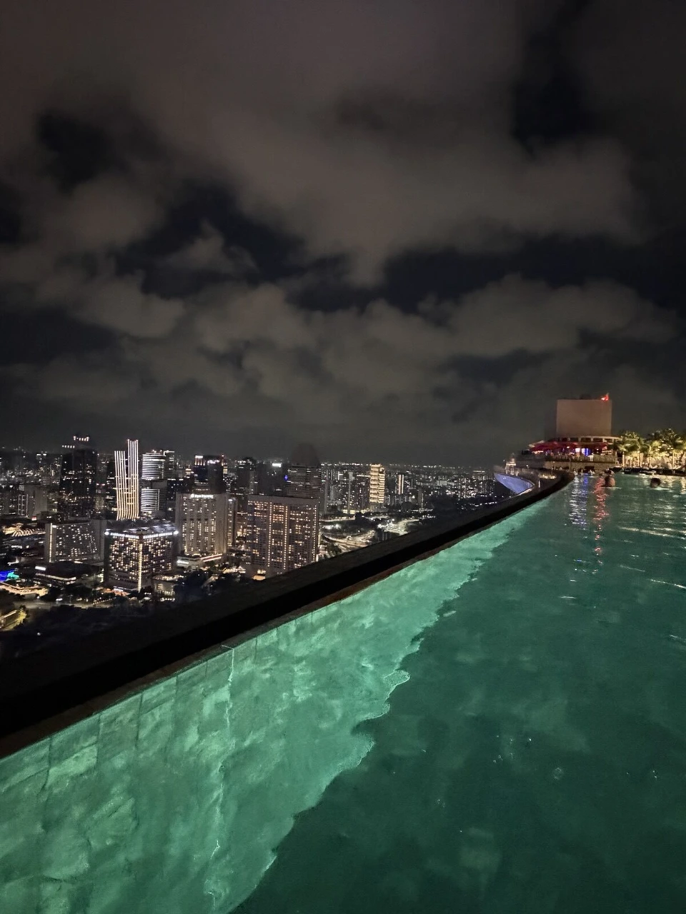 マリーナベイ・サンズの夜のインフィニティプールの縁と、その先のシンガポールの夜景