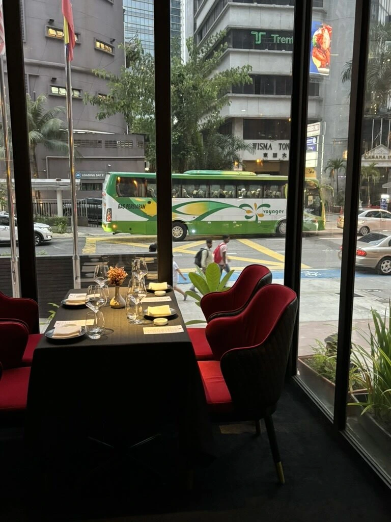 Skillet KL(旧店舗)の窓際の席。黒いテーブルクロスと赤いベルベットの椅子、窓の外の通りとバス