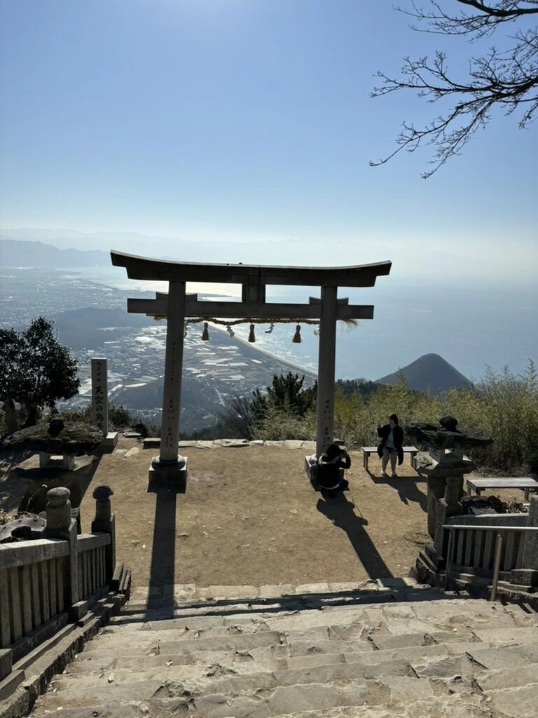 石段の上から見下ろした鳥居と灯籠。鳥居の奥に海と平野
