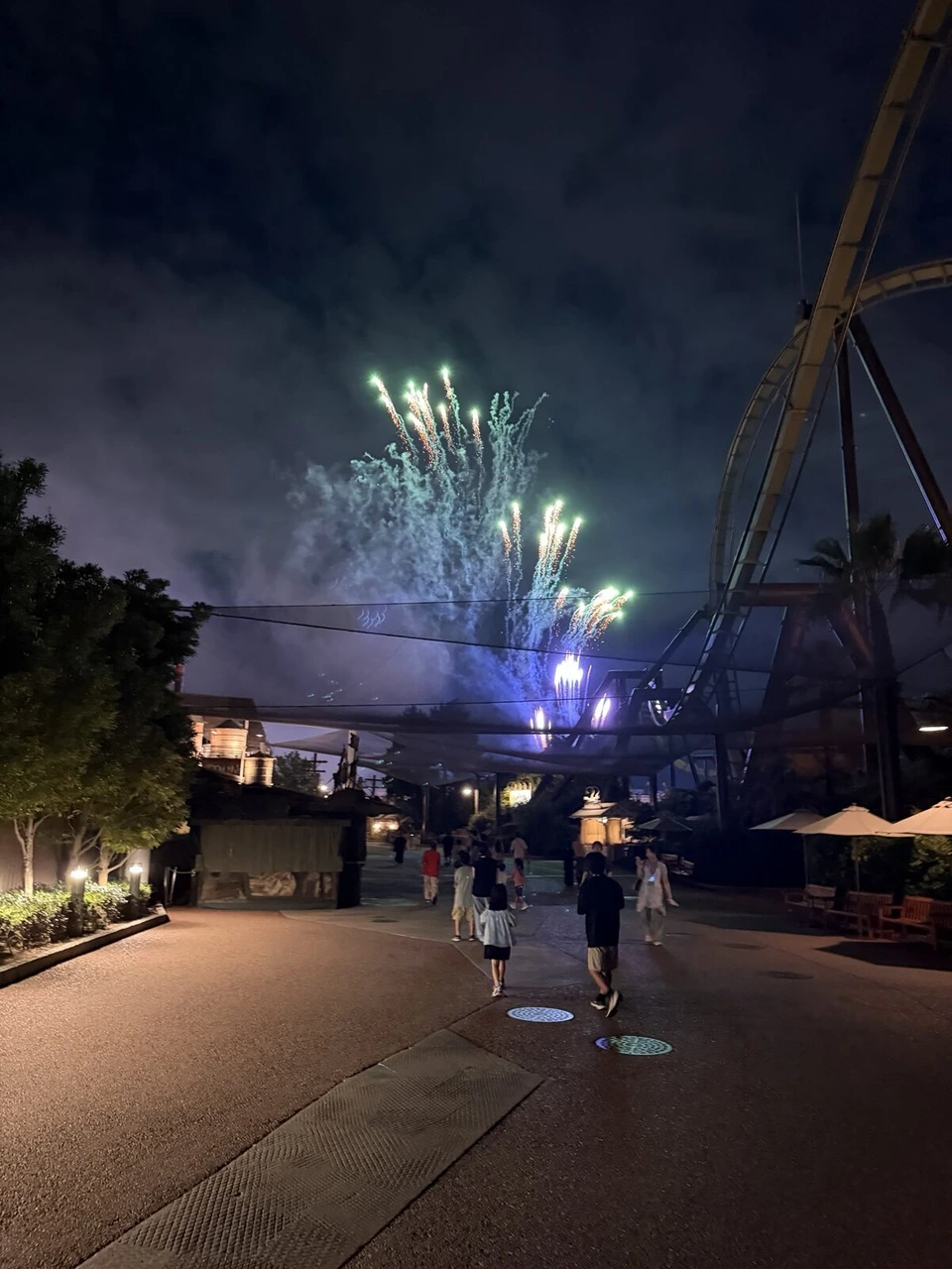 夜空に上がる緑と青の花火と、右側のザ・フライング・ダイナソーのレール
