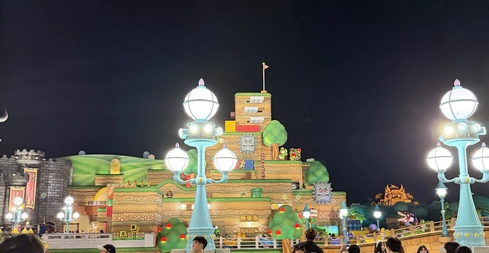 夜のスーパー・ニンテンドー・ワールド。ライトアップされたピーチ城の山と水色の街灯