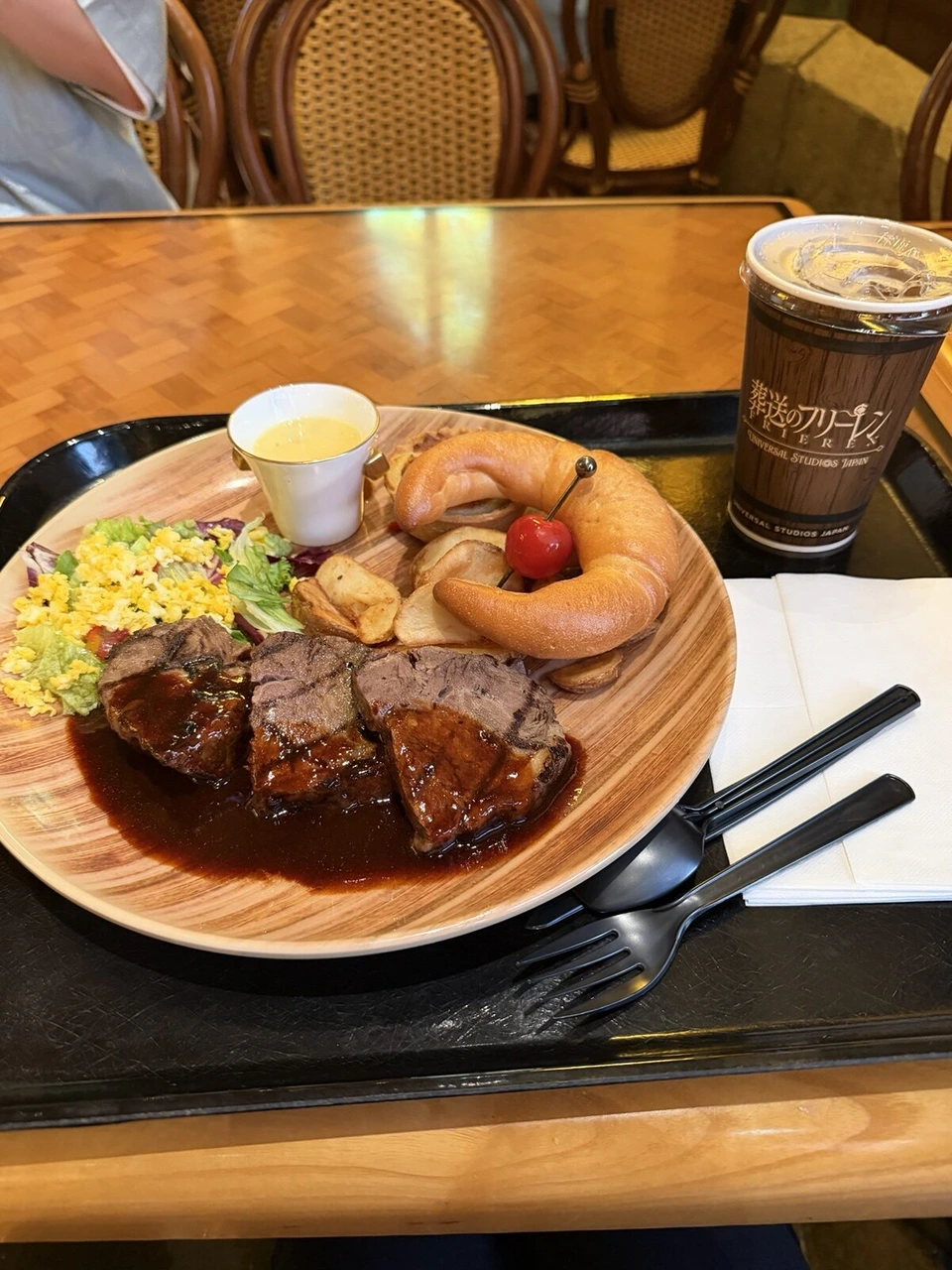 木目の皿に乗った肉料理のプレート。デミグラスソースの肉、スクランブルエッグ、ポテト、パン、スープ